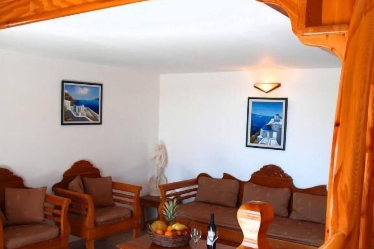 A wooden-furnished living room with a sofa, chairs, and a coffee table. There are two framed pictures on the walls.