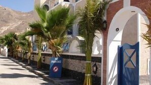 A row of hotel buildings with palm trees, a blue sign indicating no parking, and a blue gate. - Princess Santorini Villa (Santorini)