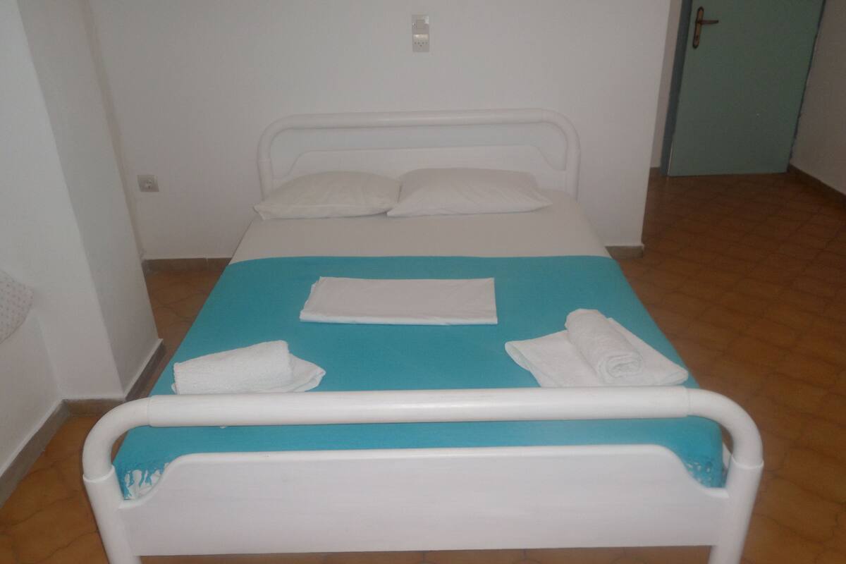 A single-bed room with a blue bedspread, white pillows, and two rolled towels.