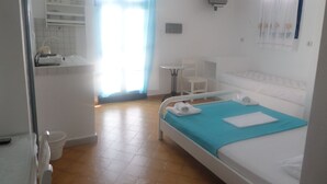 A bedroom with a bed, a small table, a chair, a TV, and a bathroom visible through an open door. - Princess Santorini Villa (Santorini)