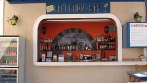 A reception bar with a counter displaying various bottles and a menu sign. - Princess Santorini Villa (Santorini)