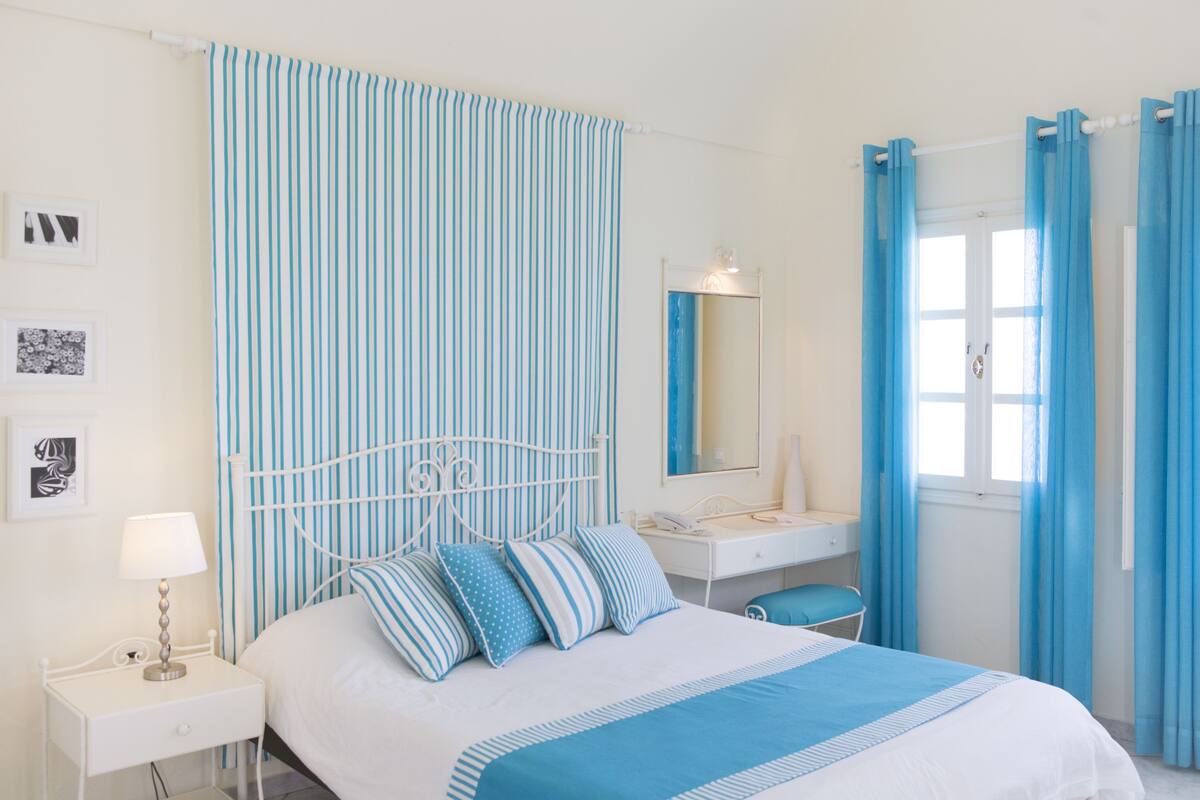 A bedroom with a bed, a bedside table, a lamp, a dresser, a mirror, and curtains.