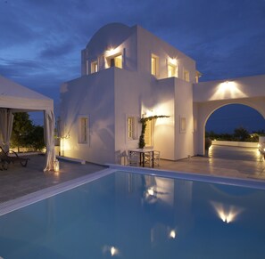 Una villa moderna con piscina, mobiliario exterior y un patio cubierto.