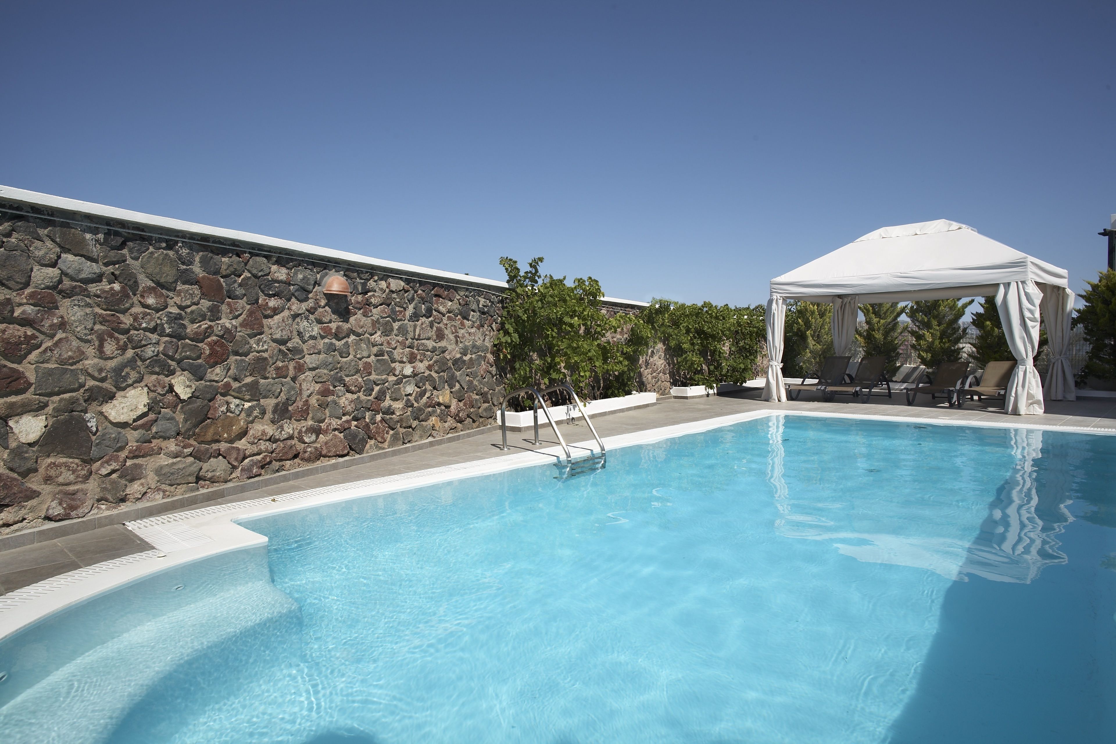 A clear blue pool with a stone wall and a white canopy.