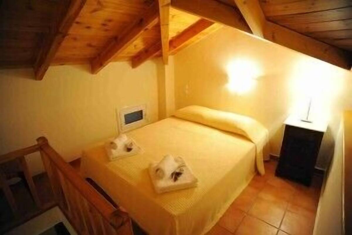 A small, cozy room with a single bed, a nightstand, and a wooden ceiling.