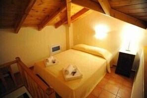 Um quarto pequeno e acolhedor com uma cama de solteiro, uma mesa de cabeceira e teto de madeira.