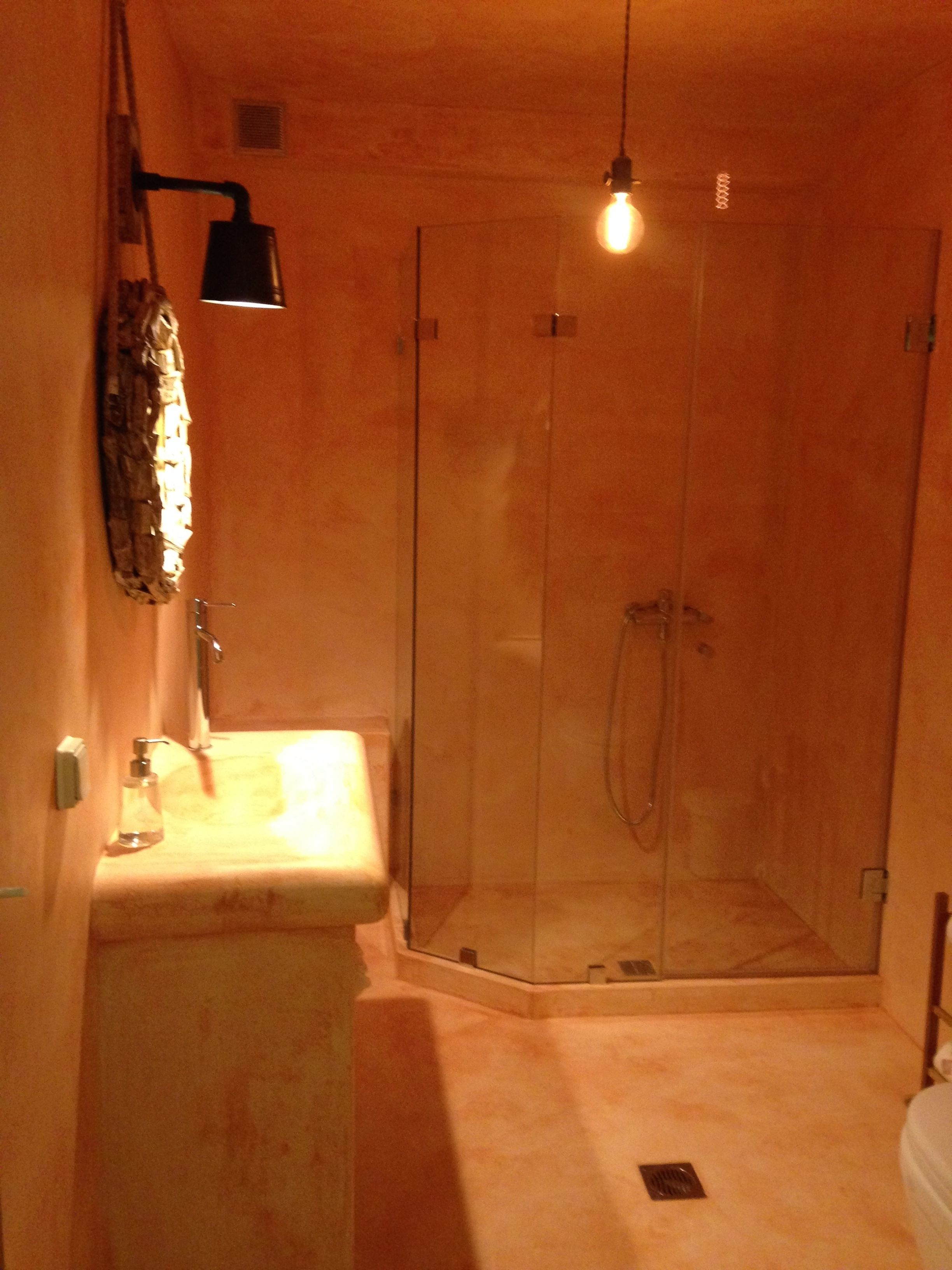 A bathroom with a glass-enclosed shower, a sink with a soap dispenser, and a hanging light fixture.