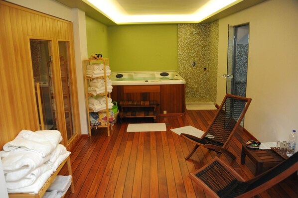 A wooden-floored room with a wooden chair, a shelf with towels, and a small table with a bottle and glasses.