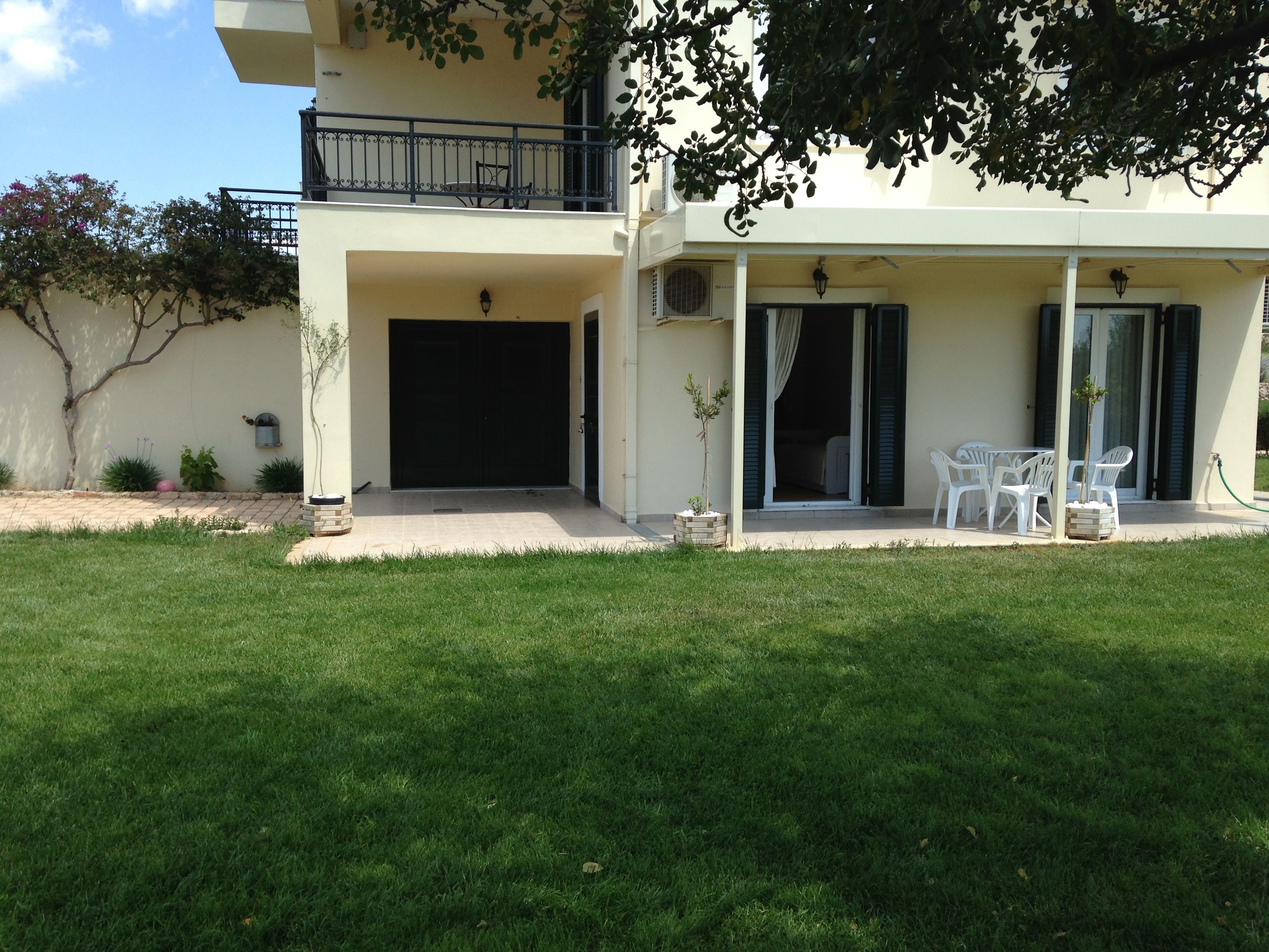 A two-story building with a covered patio area, a small garden, and a seating arrangement.