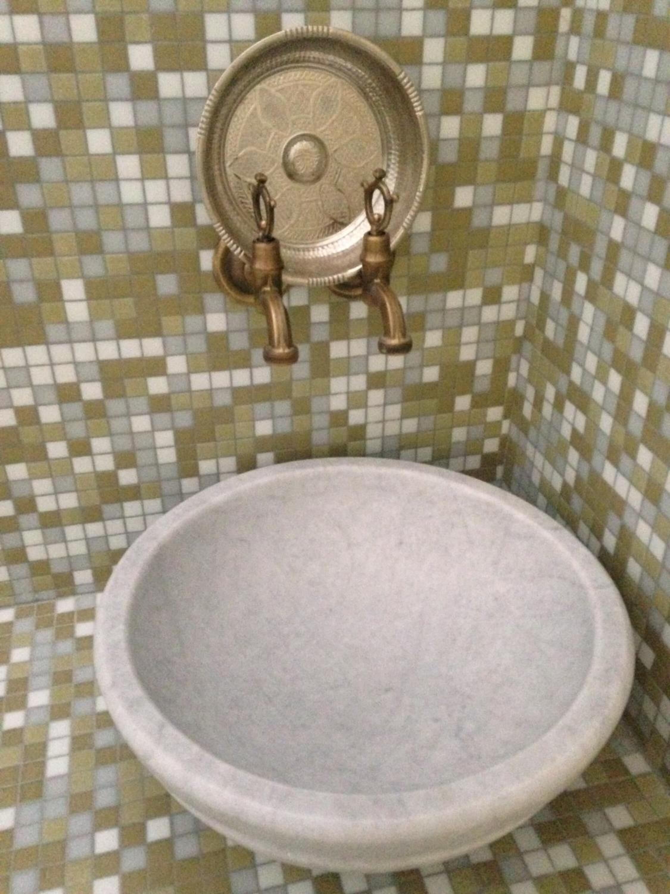A bathroom with a mosaic tile wall, a round sink, and a brass faucet.