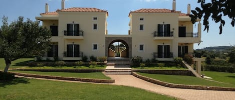 A two-story building with a central archway, surrounded by well-maintained lawns and a paved pathway leading to the entrance.