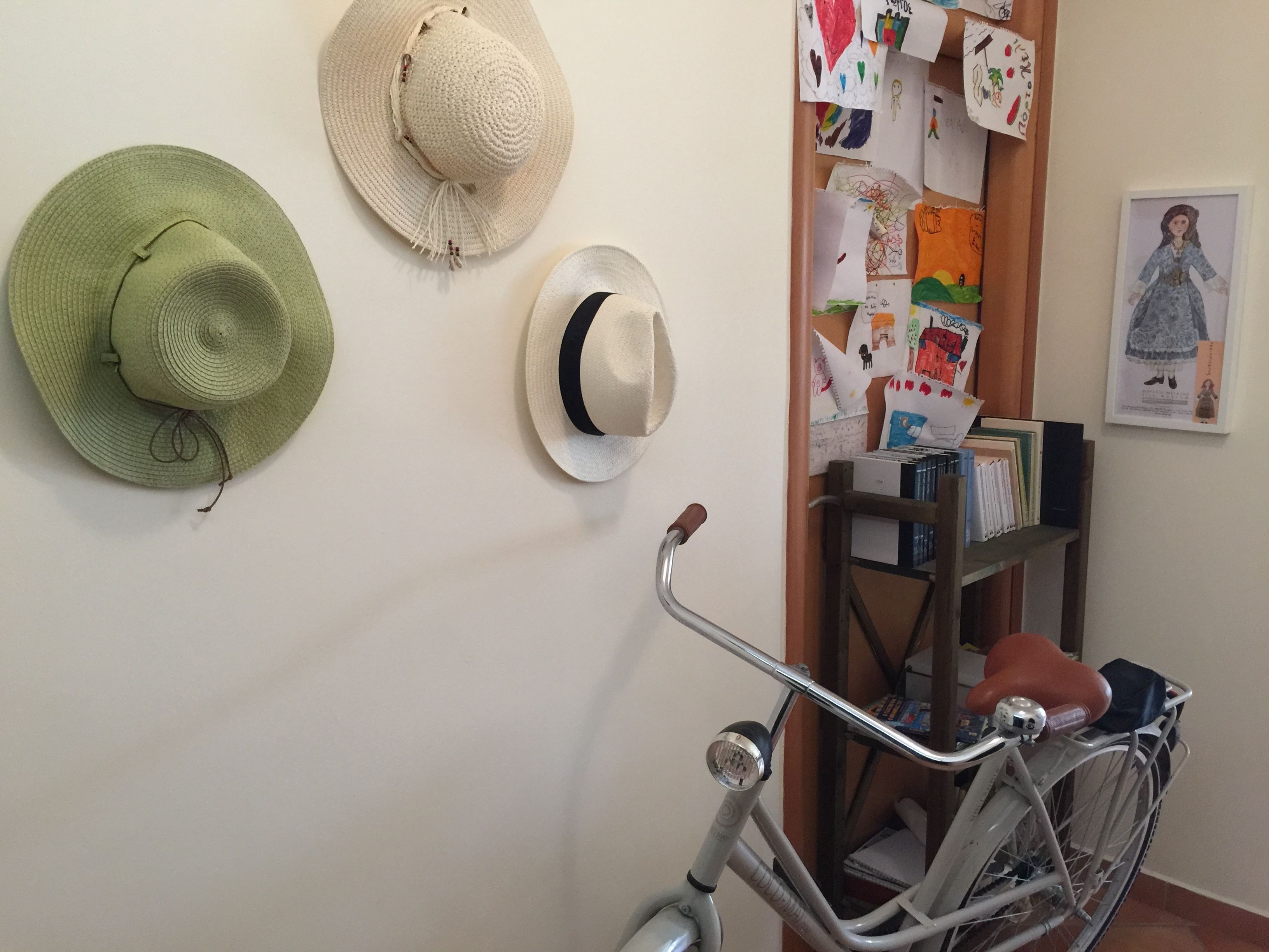 Eine Wand mit zwei Hüten, einem Fahrrad und einem Korkbrett mit Kinderzeichnungen.