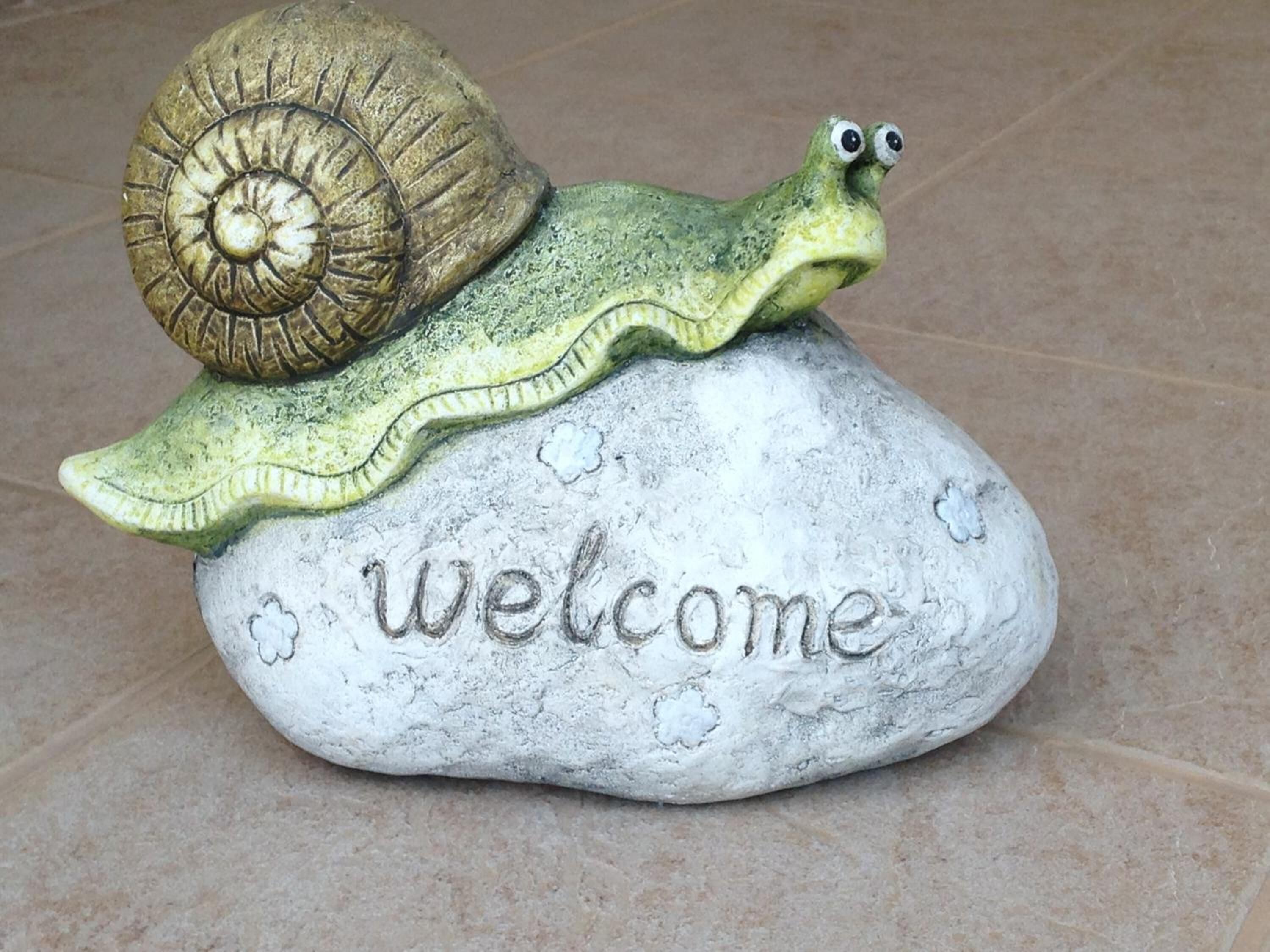A welcome sign with a snail and shell on a stone.