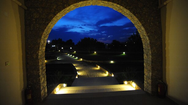Una entrada de piedra arqueada con vistas a un sendero iluminado que lleva a una carretera.
