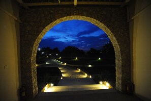 An arched stone entrance with a view of a lit pathway leading to a road. - Long View Resort & Spa Rooms & Apartments (Ermionida)