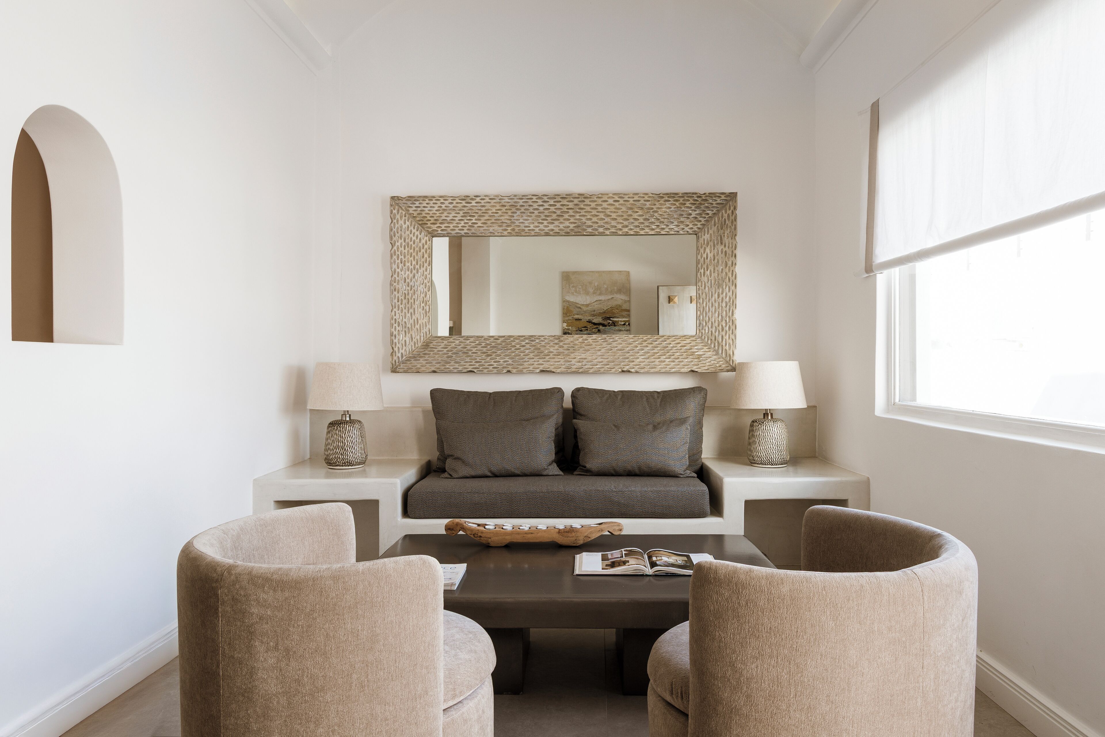 A modern room with a sofa, two armchairs, a coffee table, a lamp, and a mirror on the wall.