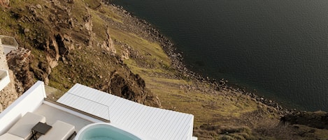 A poolside area with lounge chairs and a hot tub overlooking a rocky coastline.