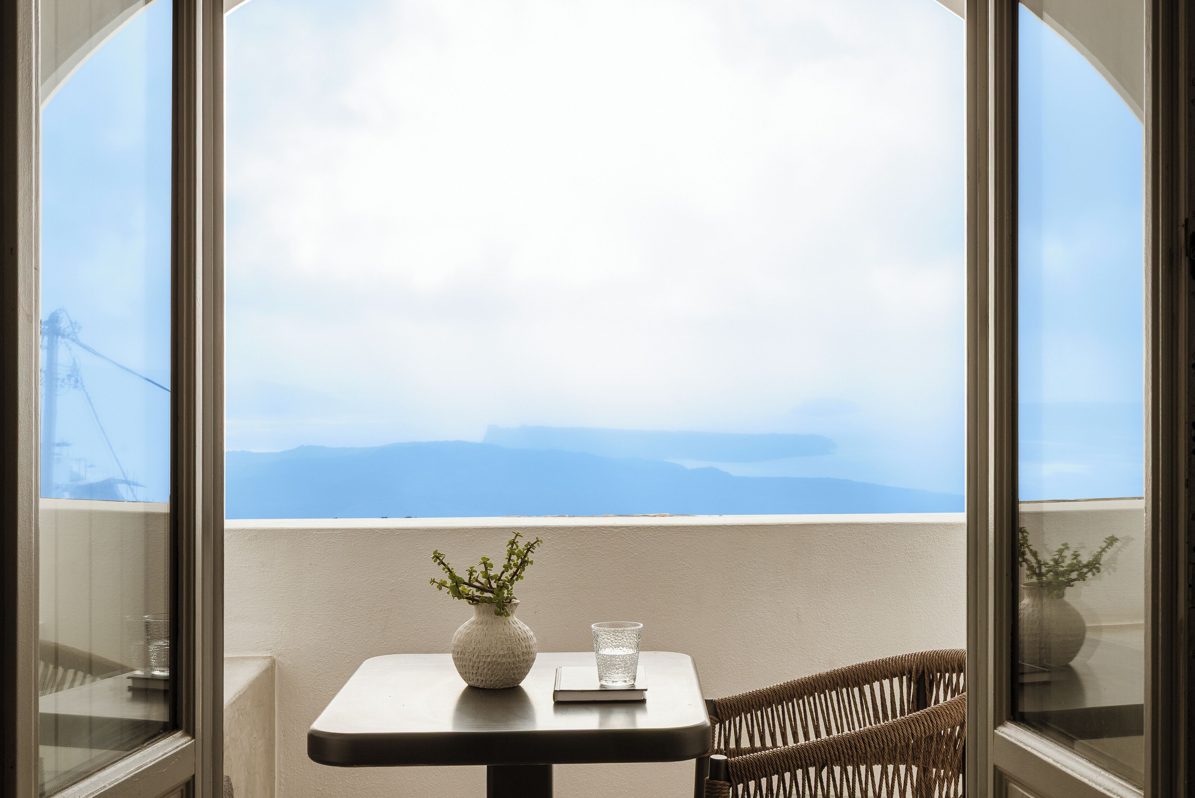 En balkon med et bord, en fletstol, en vase med planter og et glas.