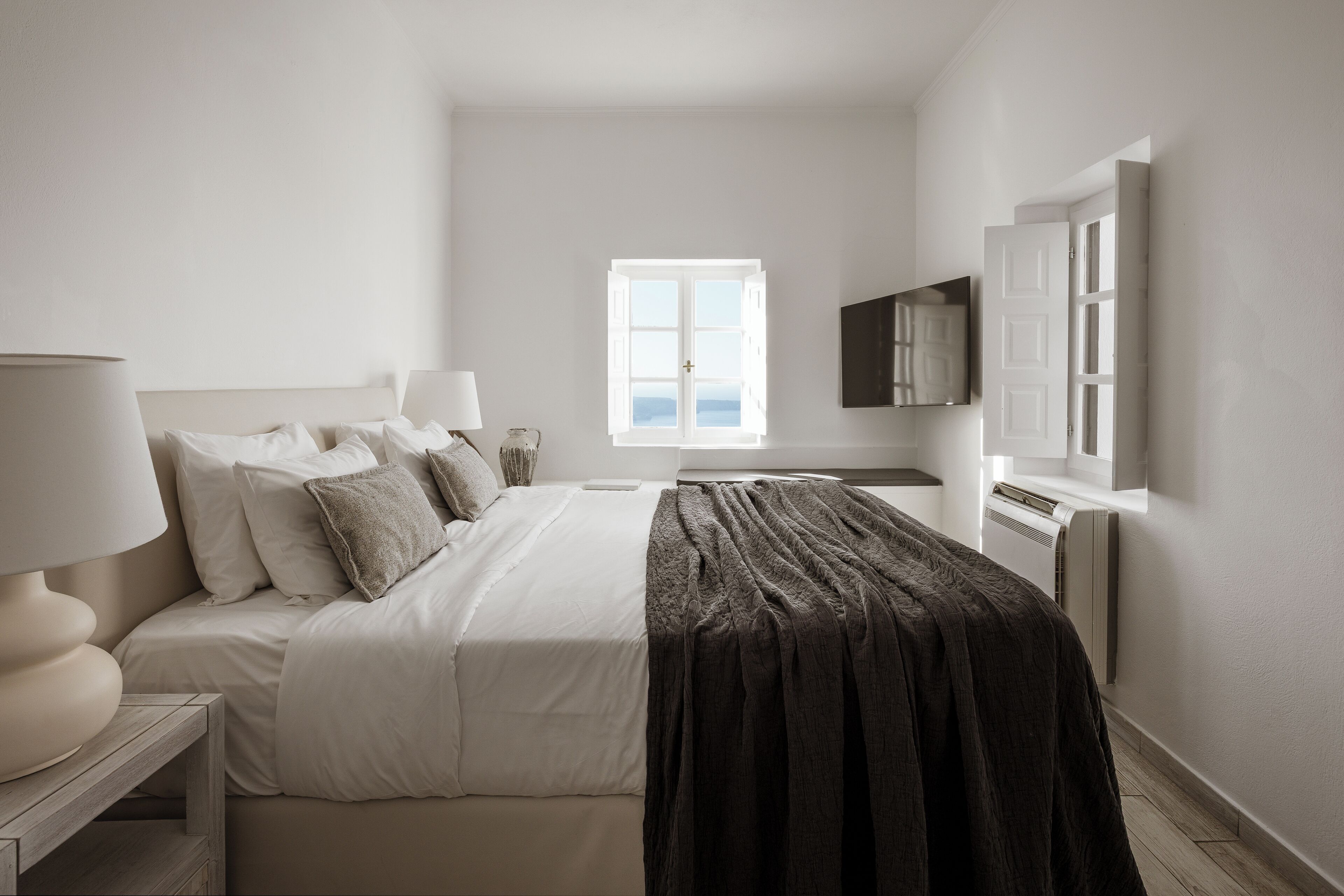 A modern bedroom with a bed, bedside lamps, a TV, and a window with a view.
