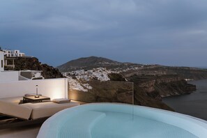 Una terraza en la azotea con piscina, zona de descanso y vistas a un pueblo costero con edificios blancos y acantilados.