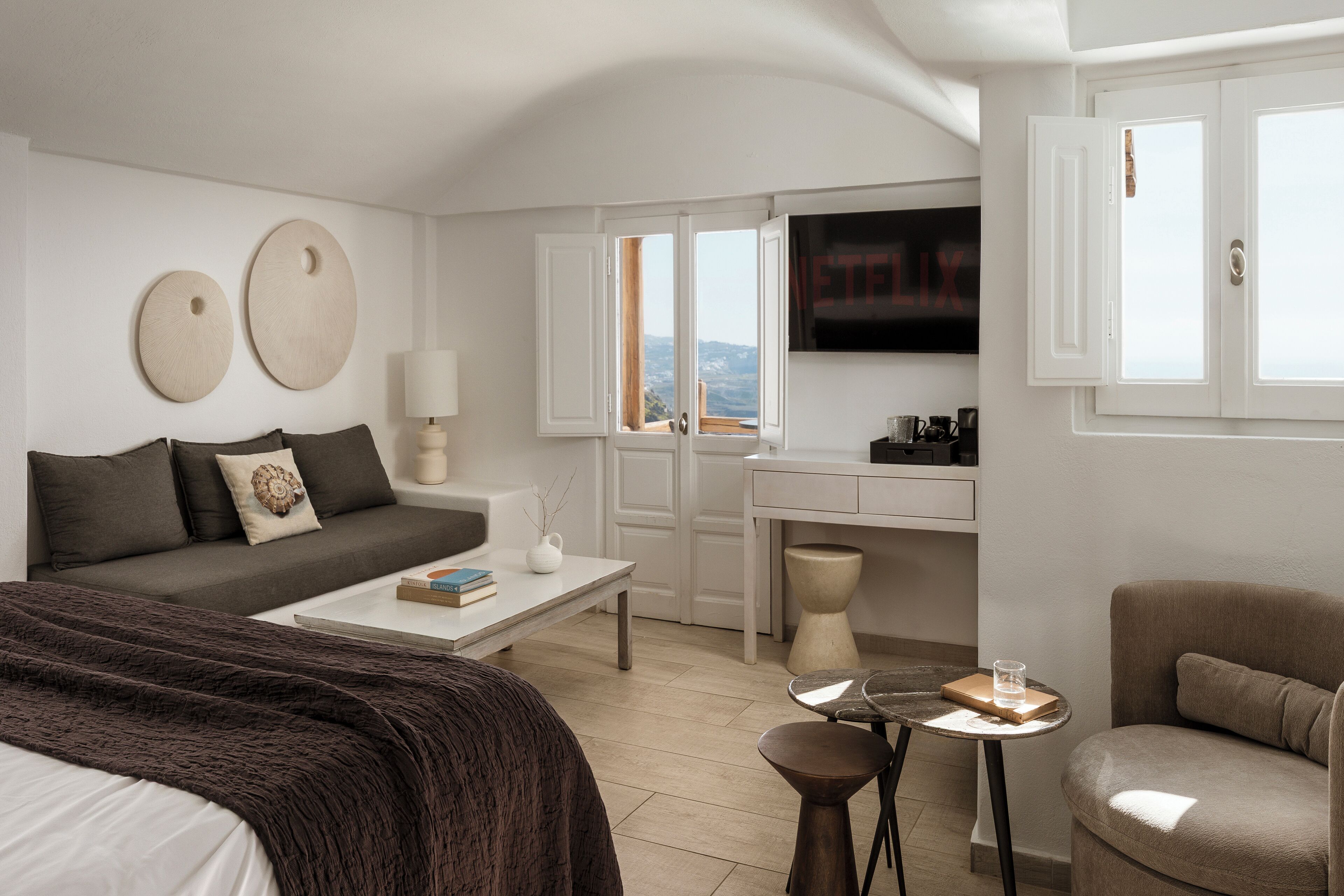 Quarto de hotel moderno com cama, sofá, mesa de centro, televisão e vista pela janela.