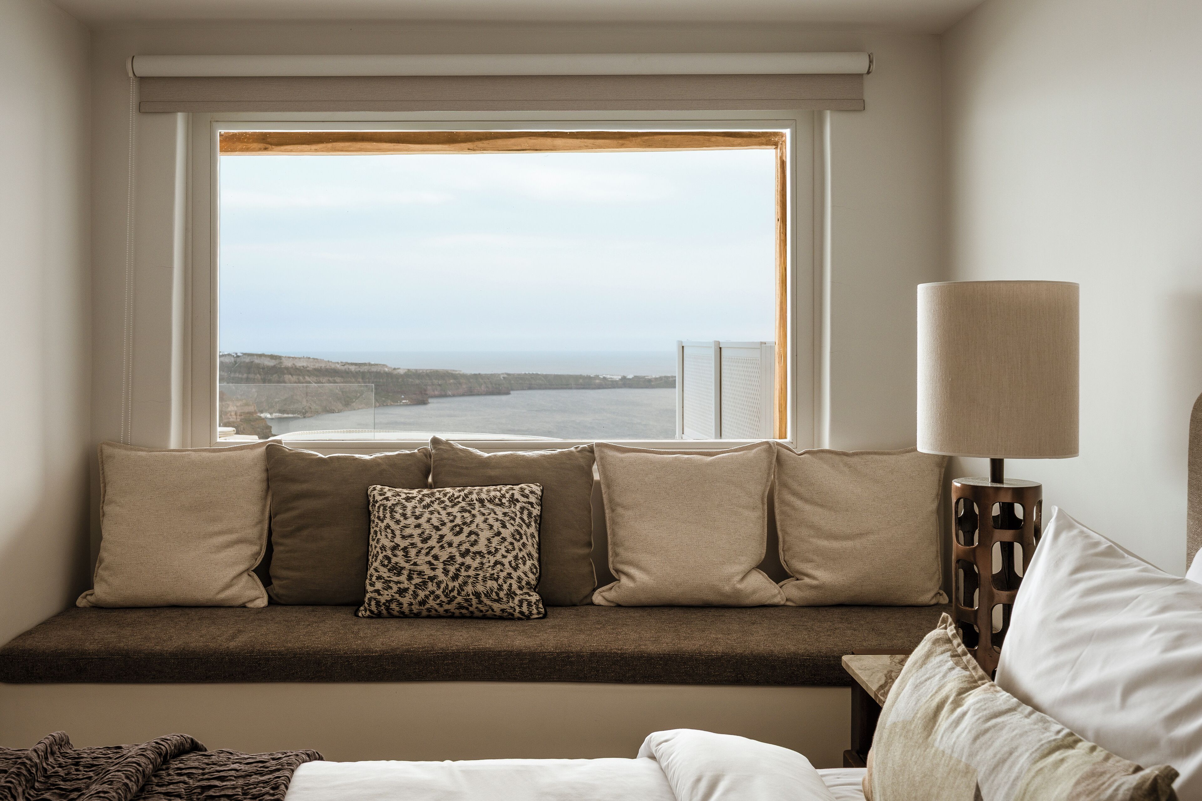 A room with a window seat, a lamp, and a view of the sea.