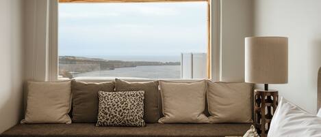 A room with a window seat, a lamp, and a view of the sea.