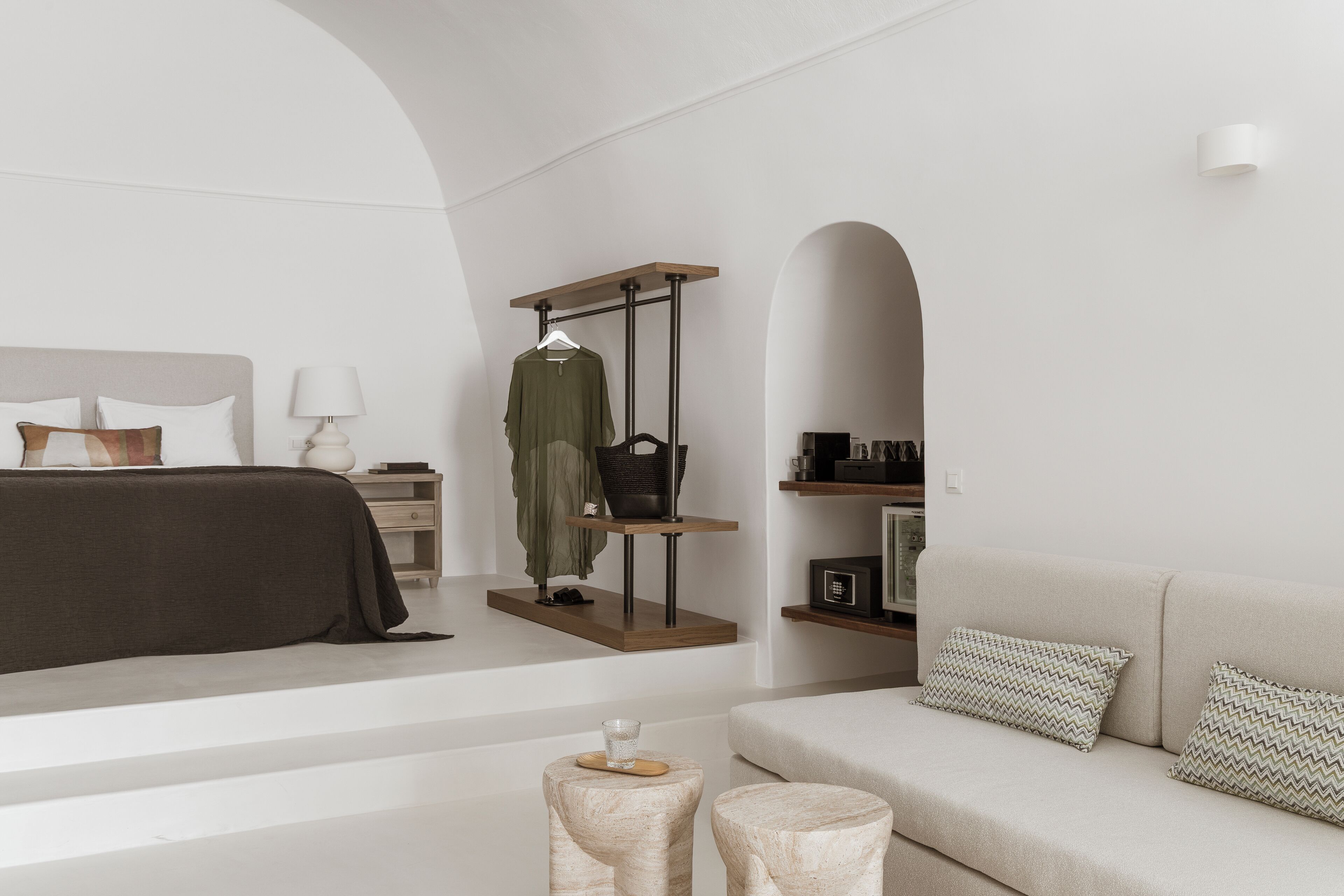 Una habitación de hotel moderna con una cama, un sofá, un perchero y una mesita con un vaso.