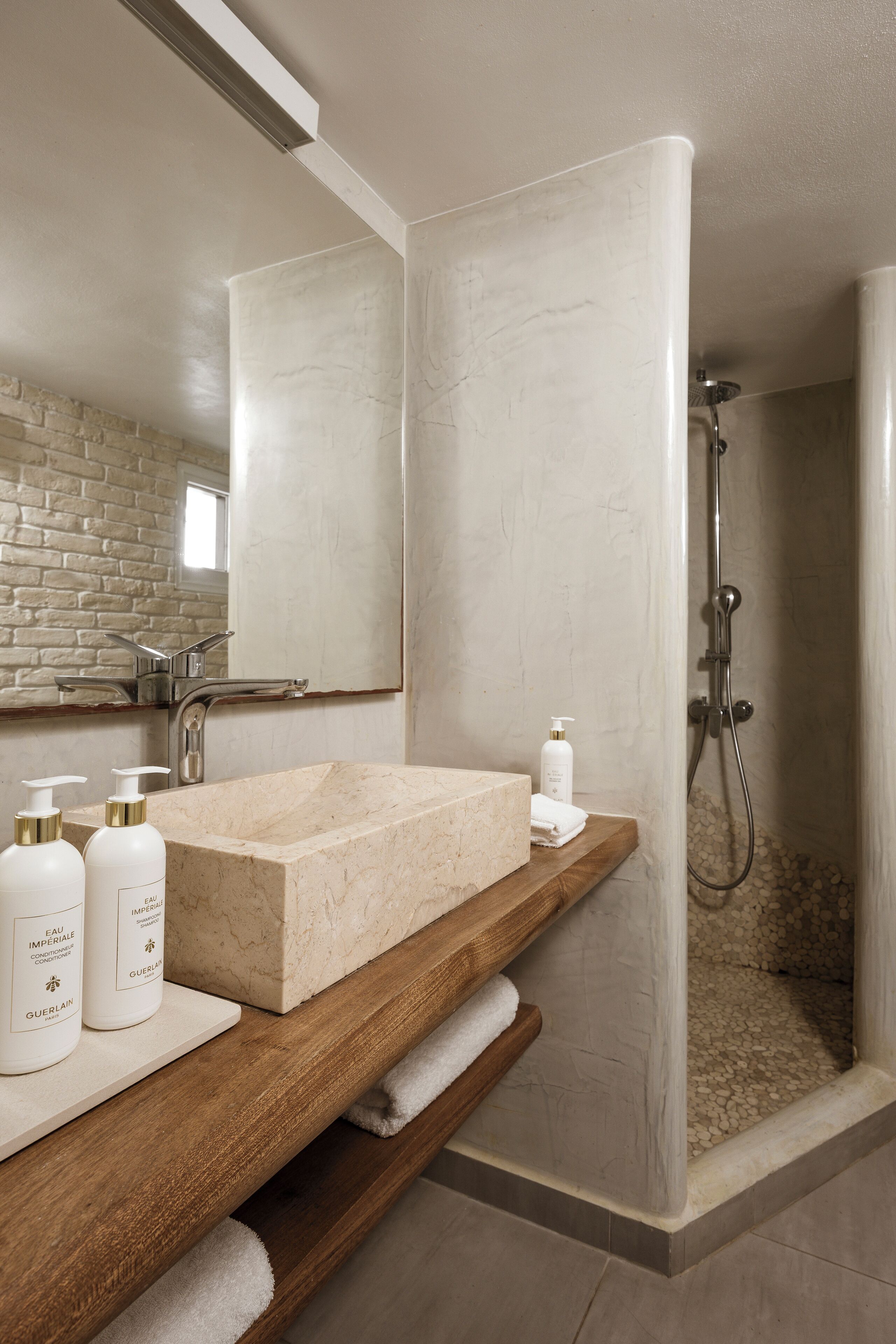 A bathroom with a marble sink, wooden shelf, and a shower area.