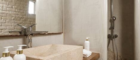 A bathroom with a marble sink, wooden shelf, and a shower area.