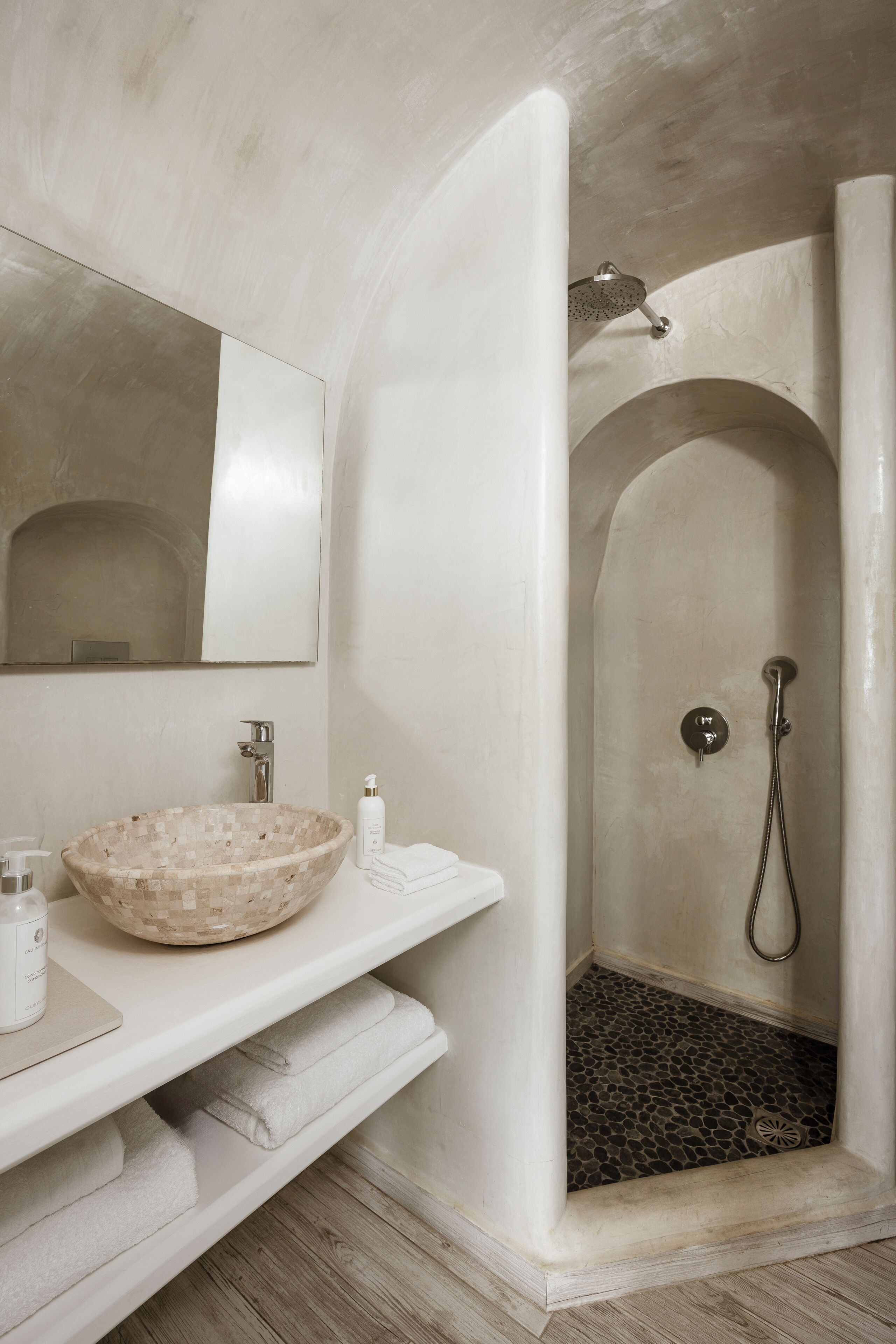 Un baño con lavamanos de mosaico, ducha con pared curva y espejo sobre el lavamanos.
