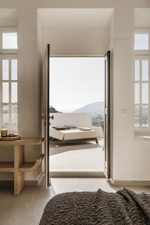 A bedroom with a bed, a wooden nightstand, a window, and a view of the outdoors.