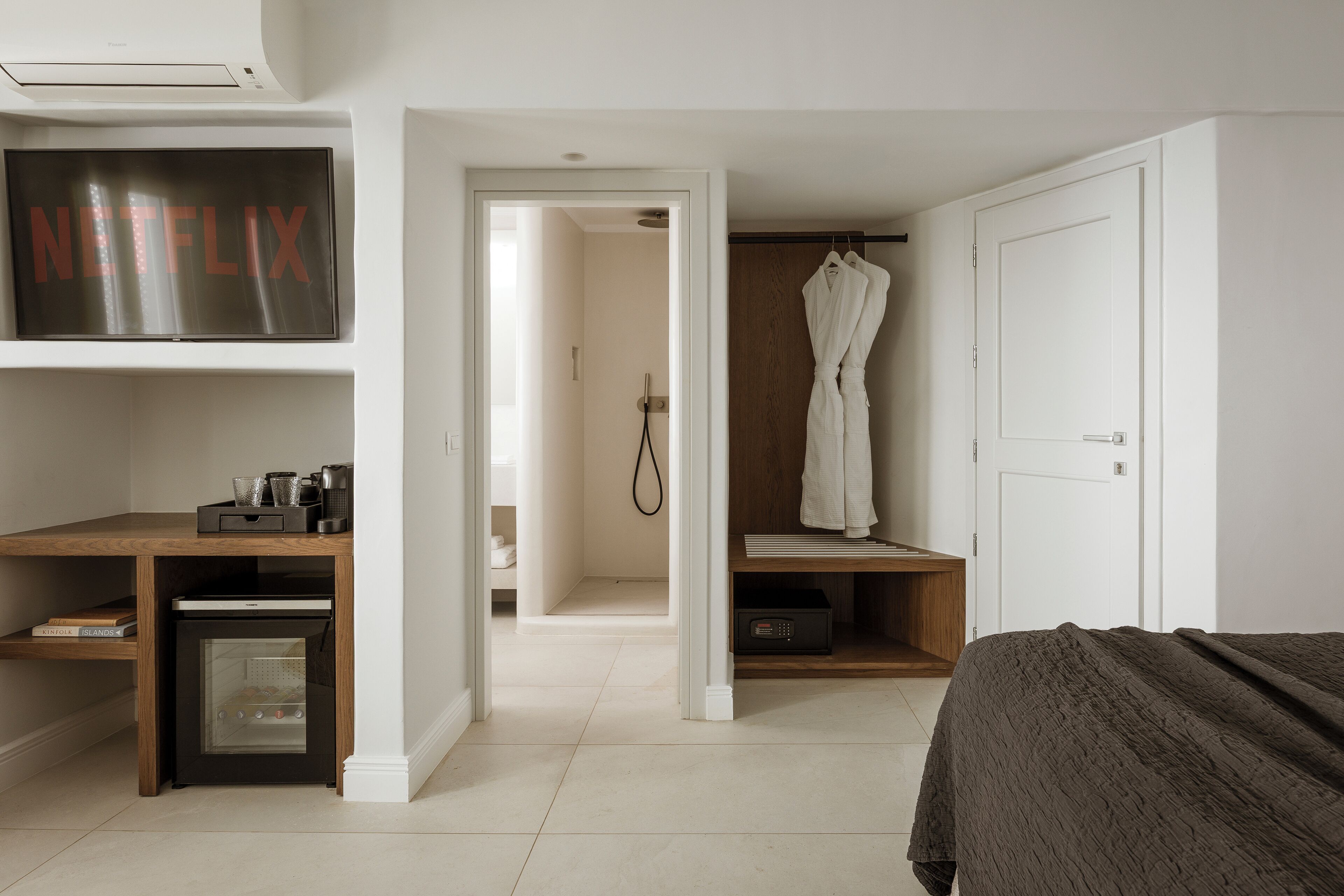 A bedroom with a bed, a TV mounted above a desk, a walk-in closet, and a door leading to a bathroom.