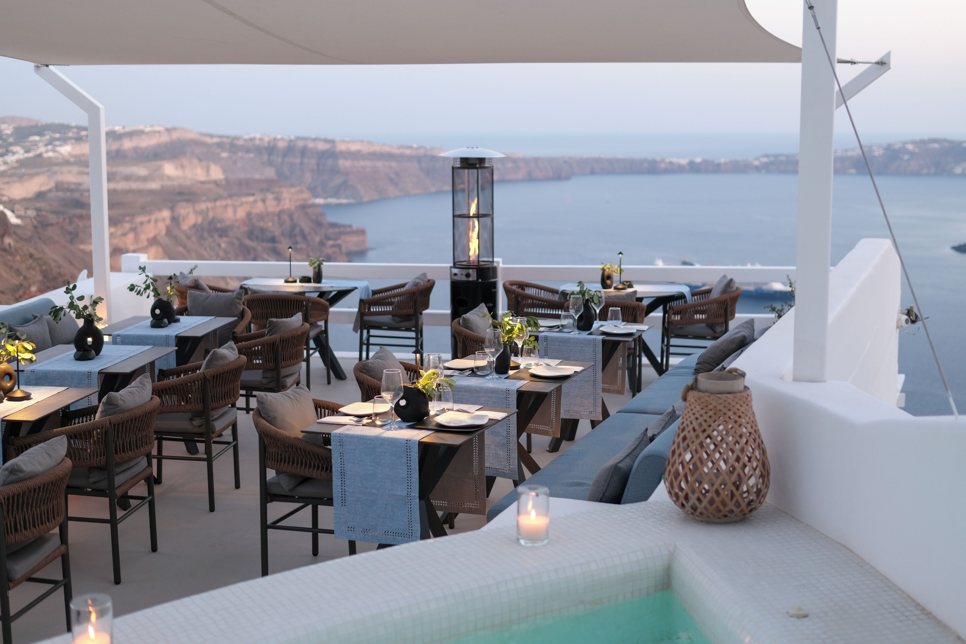 A terrace with wicker furniture, a table with a candle, and a view of the ocean and cliffs.