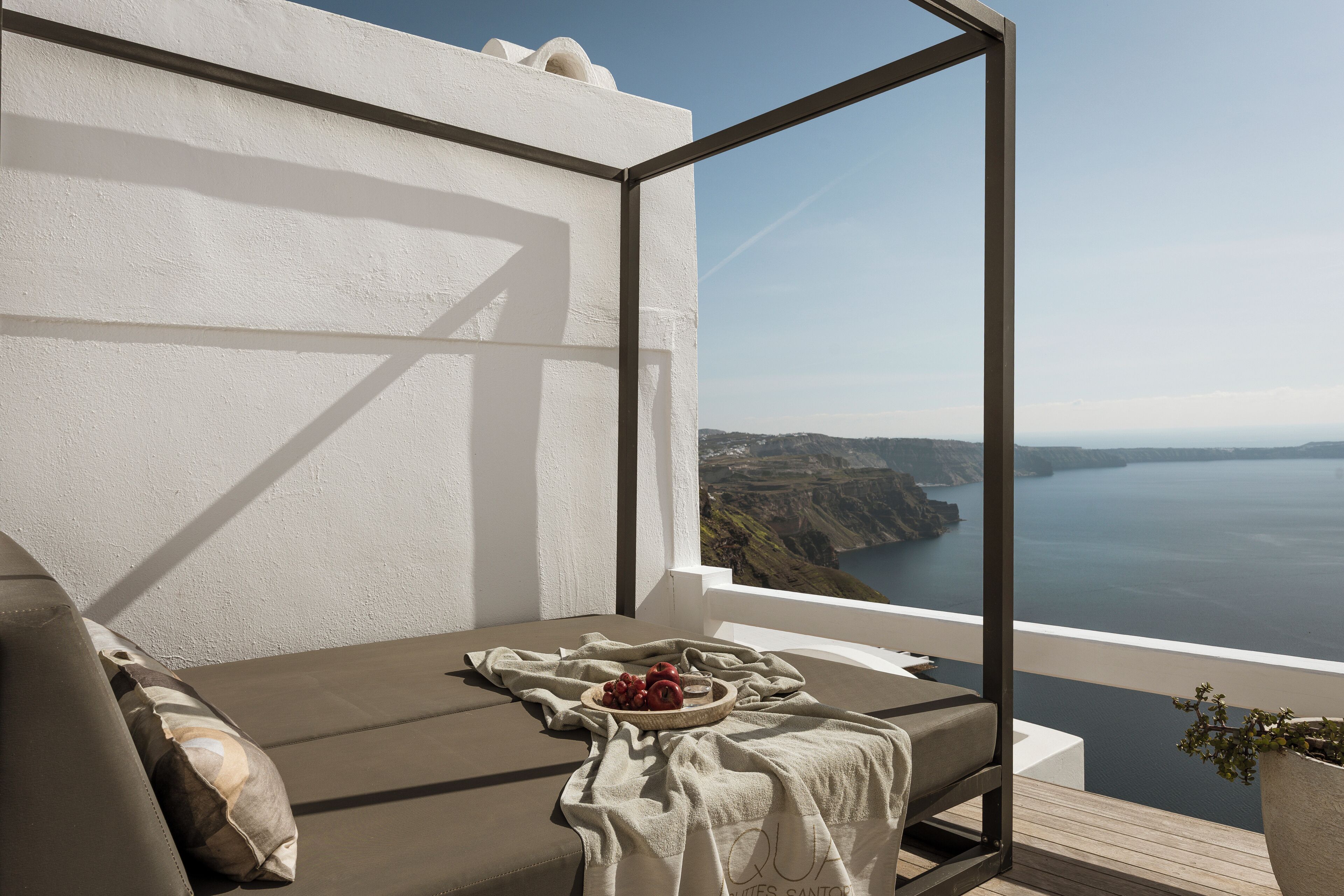 Ein Balkon mit Blick auf die Küste, eine gepolsterte Sitzecke und eine Schale mit Obst.