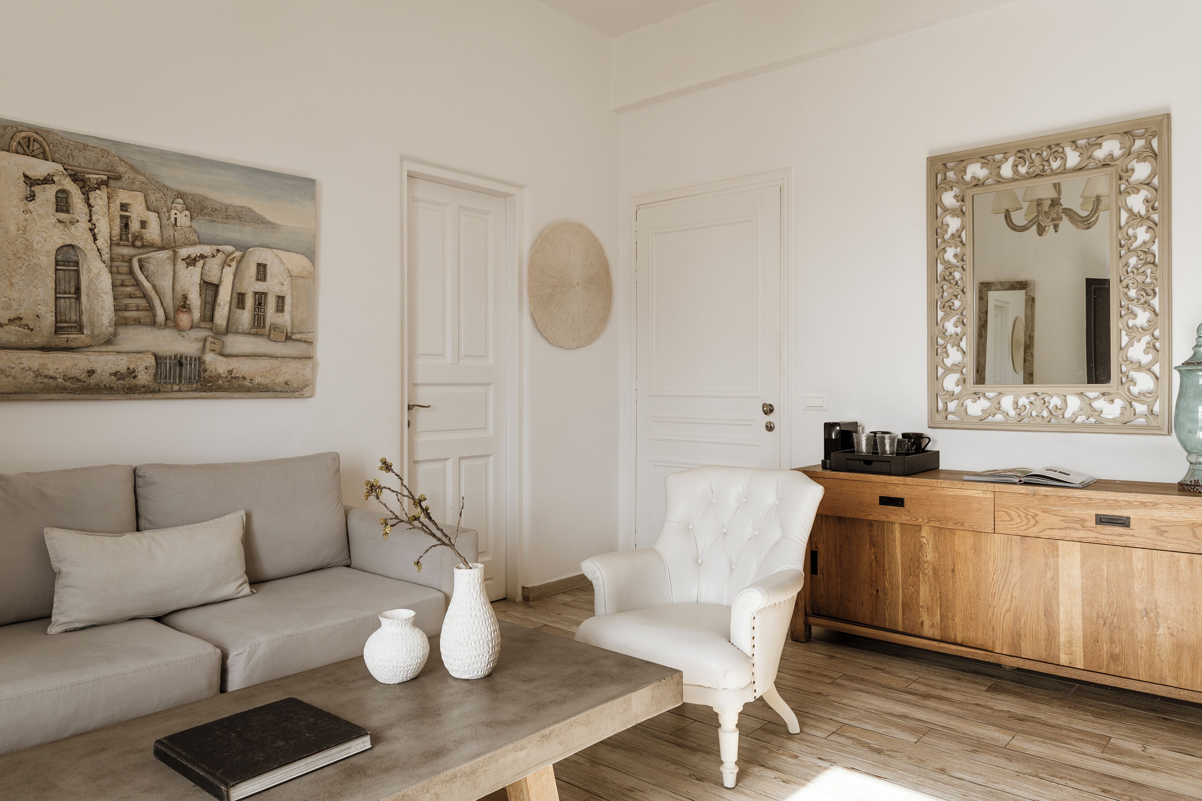 Una sala de estar con un sofá, un sillón, una mesa de centro y un cuadro de un pueblo costero.