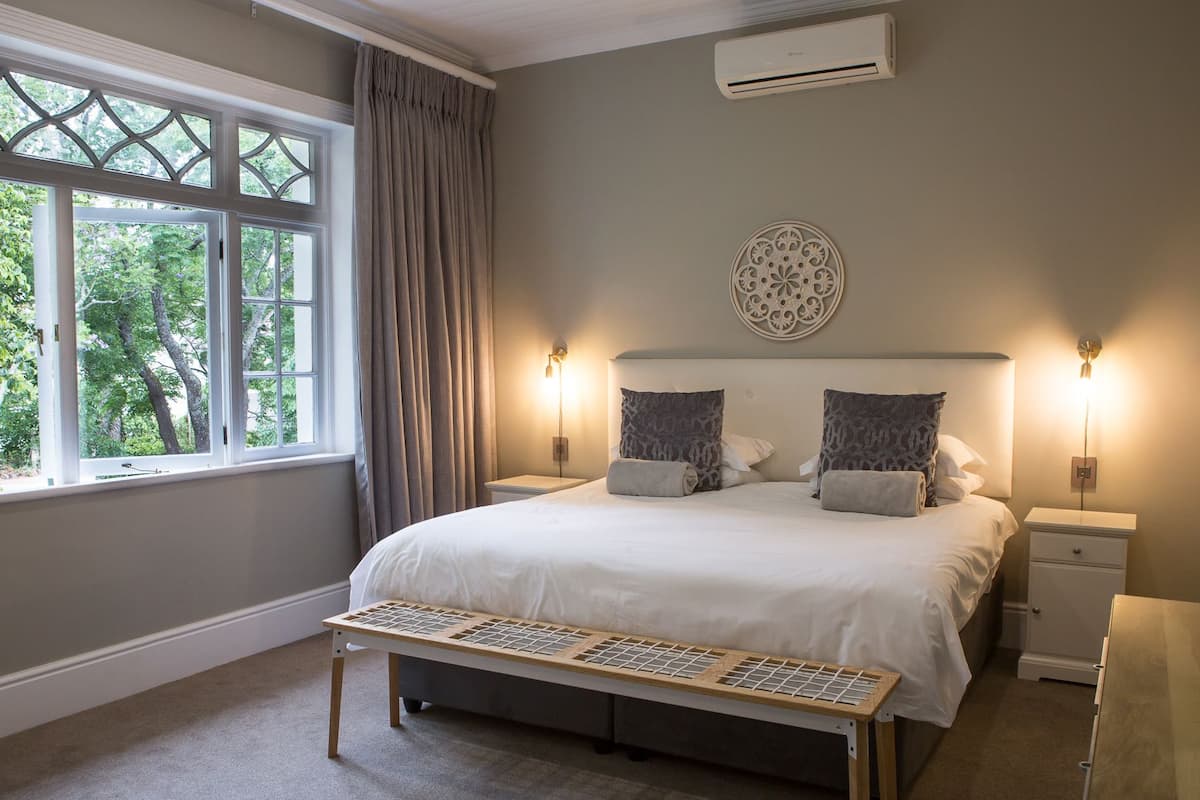 Ein Schlafzimmer mit einem großen Bett, zwei Nachttischen, einer Bank, einem Fenster mit Vorhängen und einer Klimaanlage.