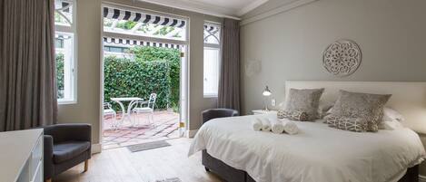 A bedroom with a large bed, a desk, and a chair. There is a window with curtains, a door leading to an outdoor area, and a wall-mounted air conditioner.