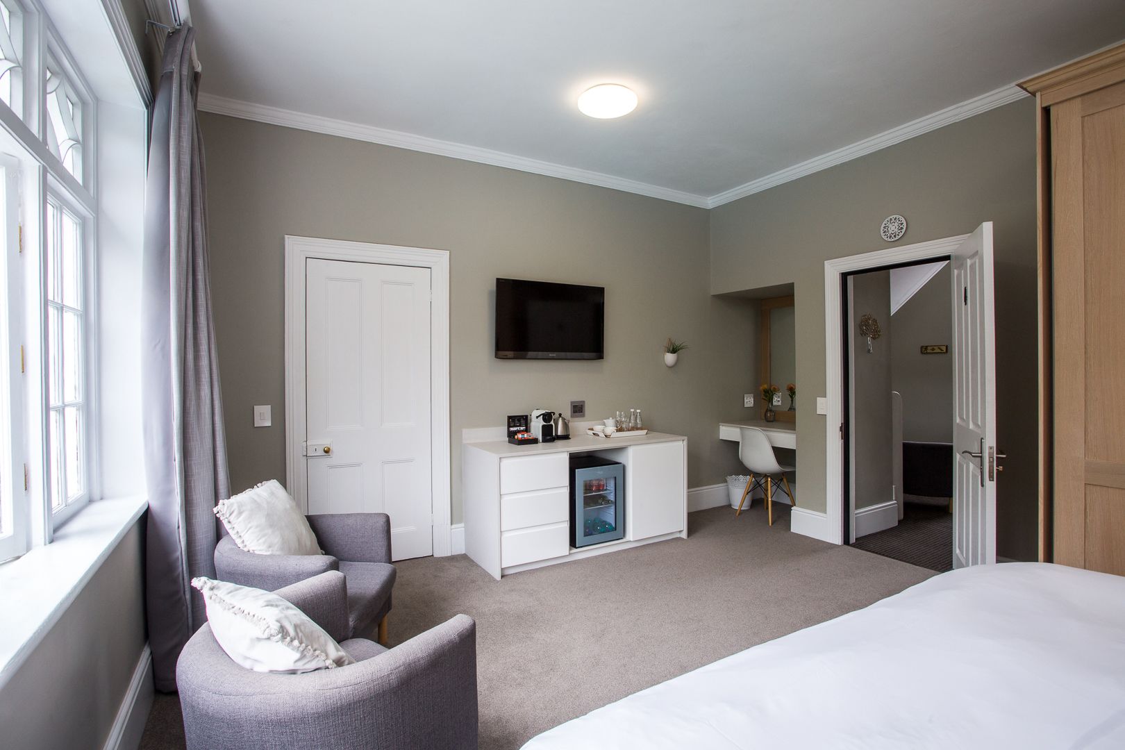 A hotel room with a bed, a desk, a chair, a TV, and a door.