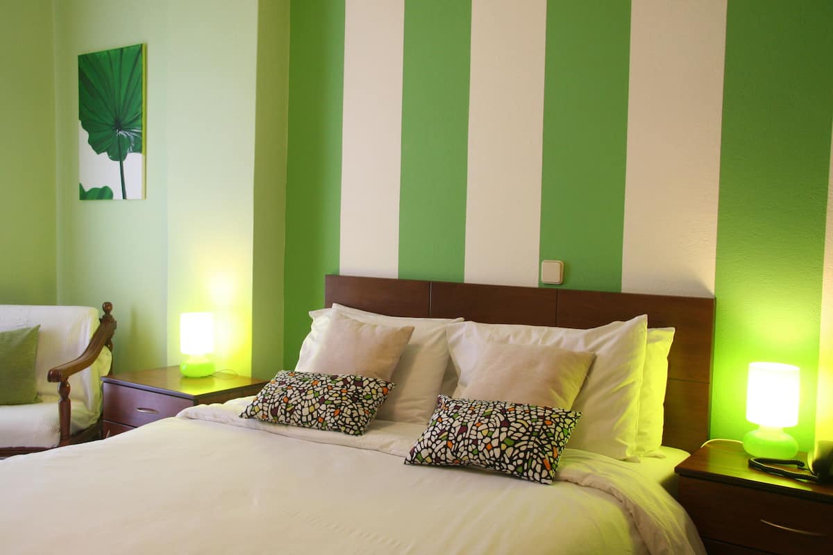 A hotel room with a bed, two bedside tables, a nightstand, and a green-striped wall.