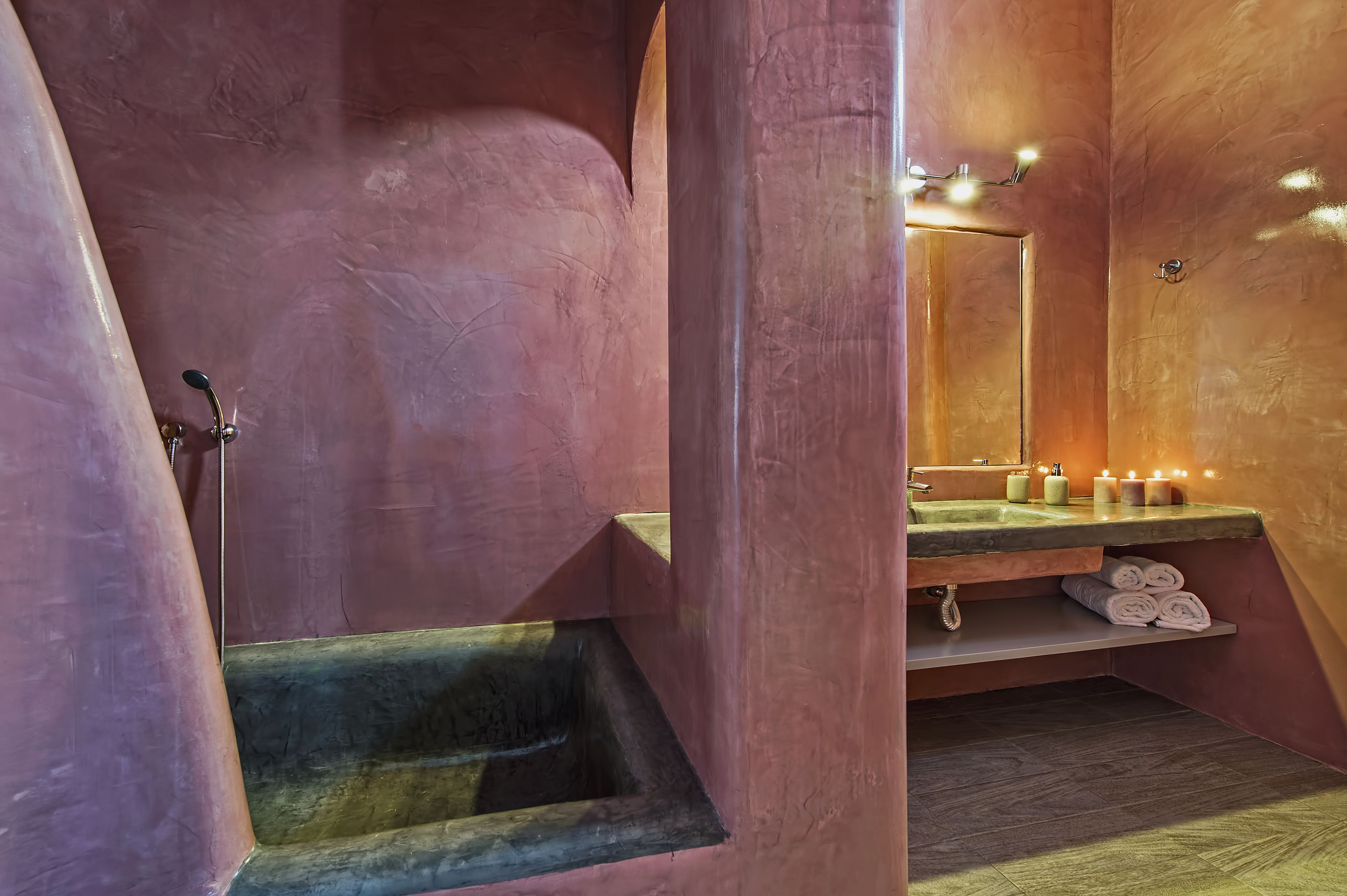 A bathroom with a pink wall, a sink with candles, and a mirror.