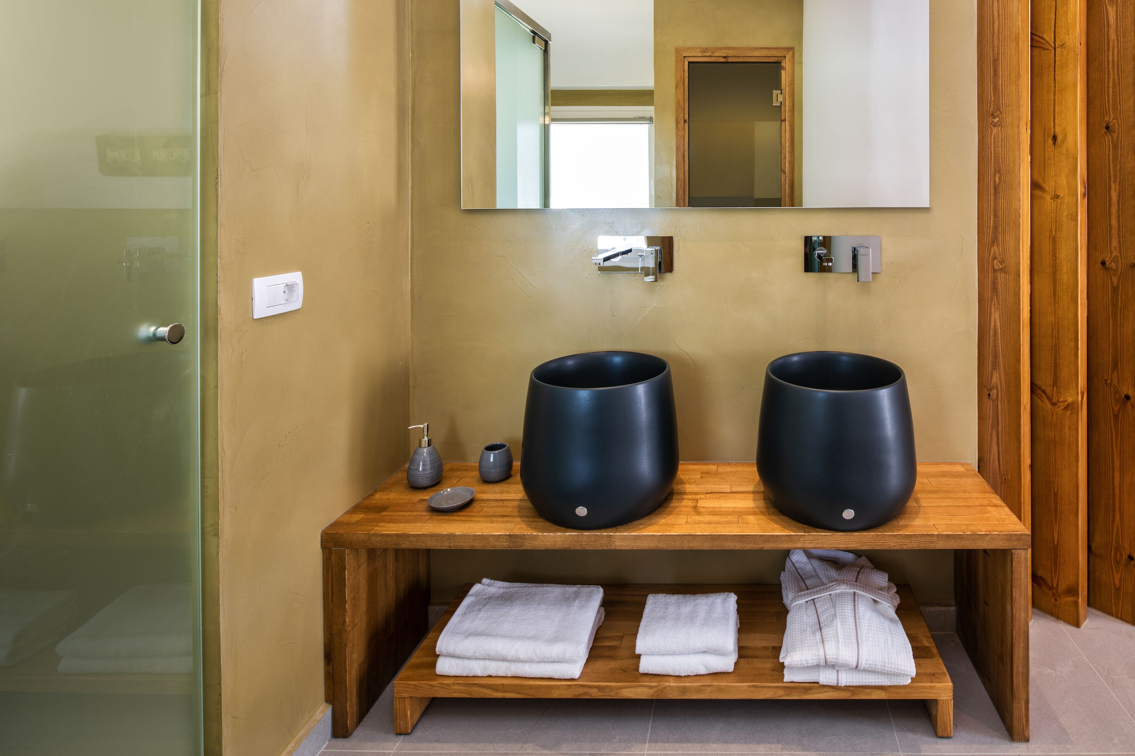 A bathroom with two black sinks, a wooden vanity, a mirror, and two towels on a shelf.