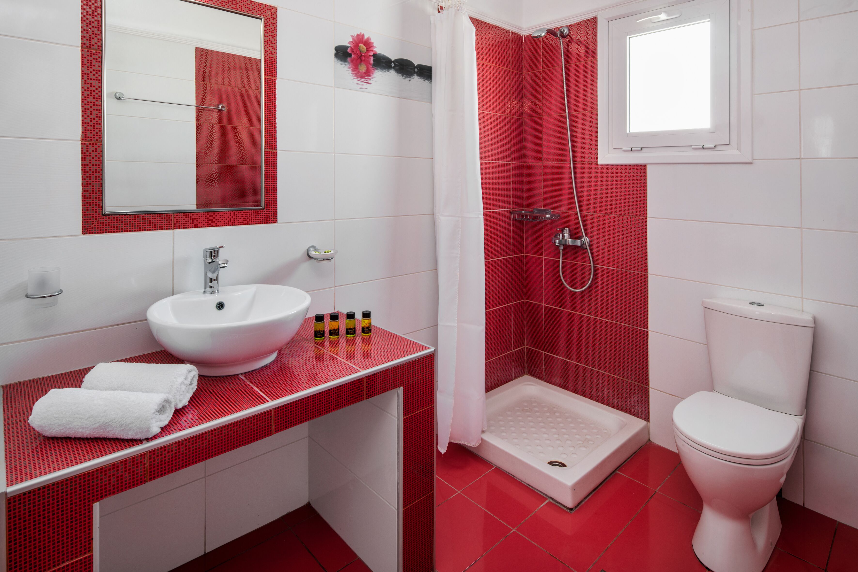 A bathroom with a white sink, red tiled walls, a white toilet, and a shower area.