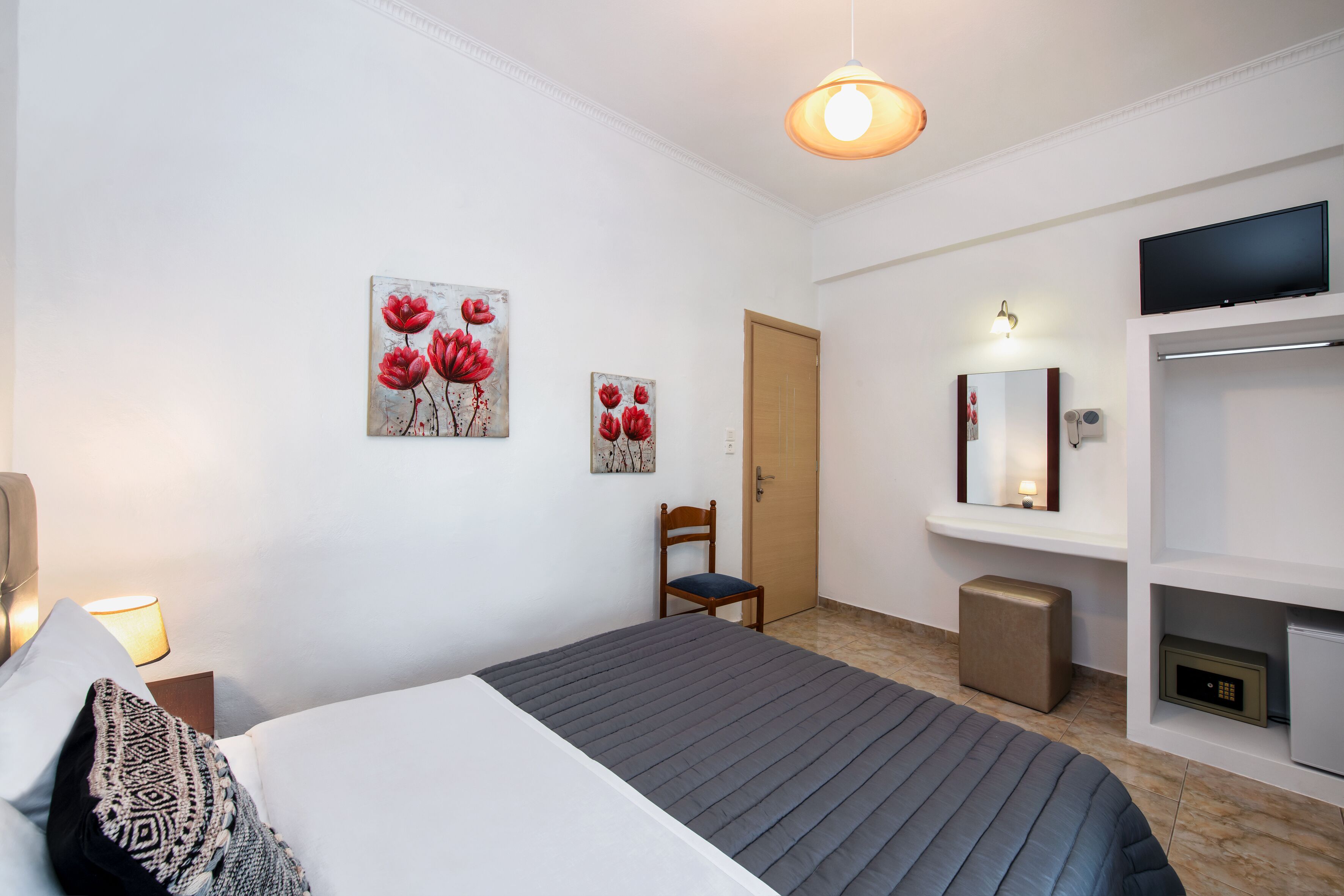A hotel room with a bed, a chair, a TV, a mirror, and artwork on the walls.
