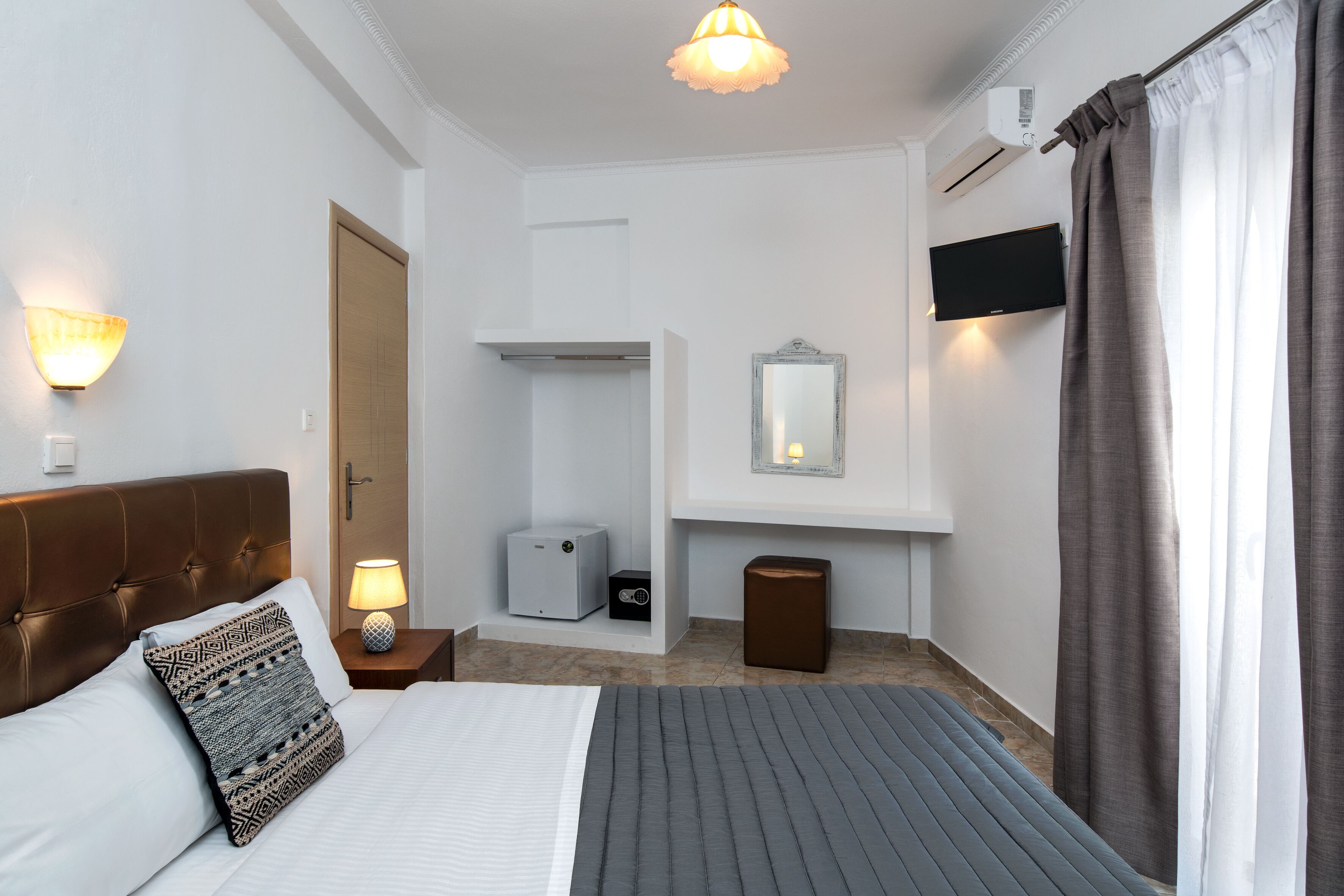 Habitación de hotel con cama, lámpara de noche, aire acondicionado, televisión y espejo.