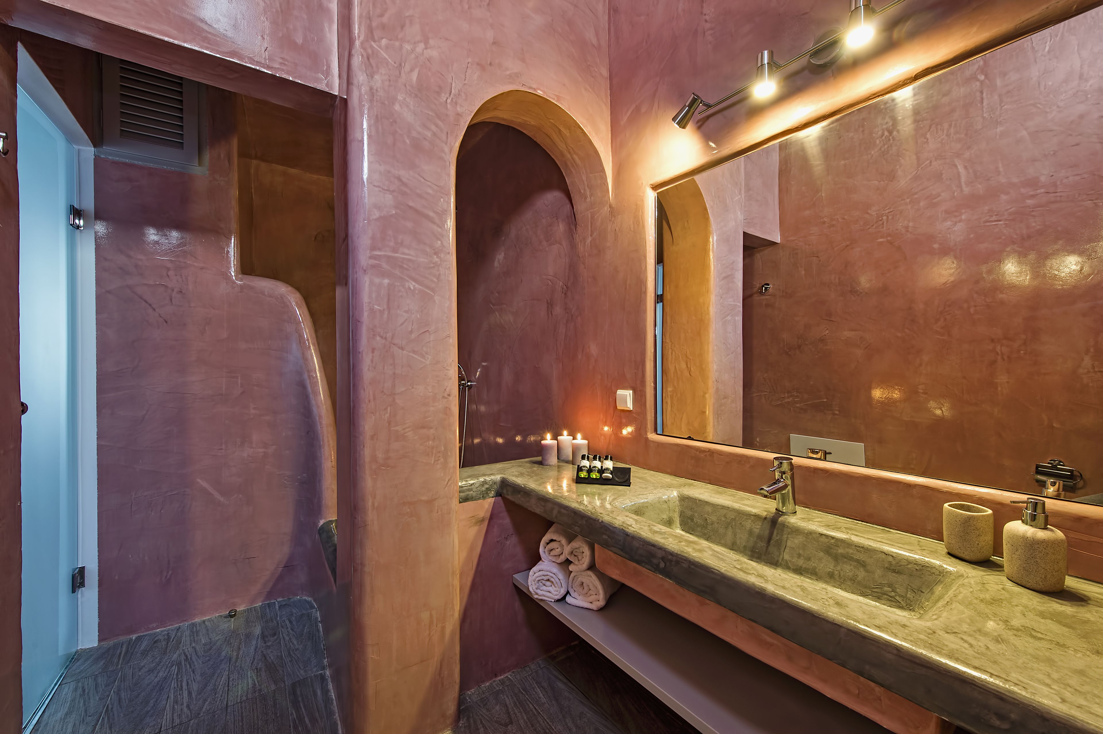 Un baño con un espejo grande, un lavabo con encimera de mármol y toallas enrolladas ordenadamente en un estante.