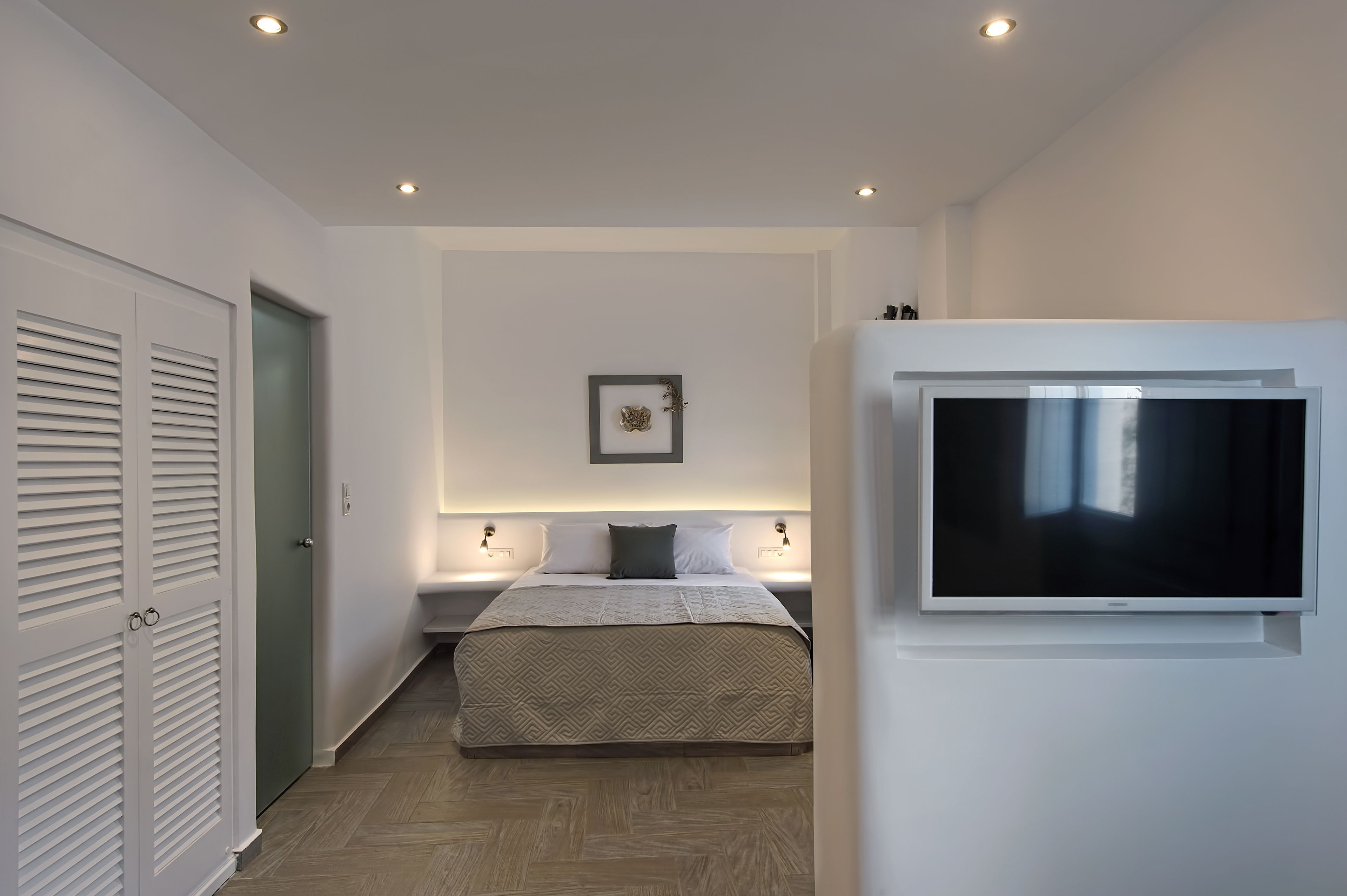 Een moderne slaapkamer met een bed, nachtlampjes, een televisie en een deur met verstelbare luiken.