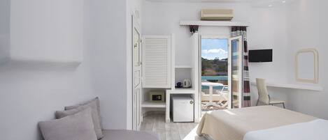 A modern hotel room with a bed, a sofa, a TV, a small table, and a balcony with a view.