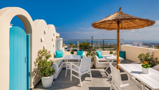 An outdoor terrace with white furniture, a blue door, and a view of the sea.