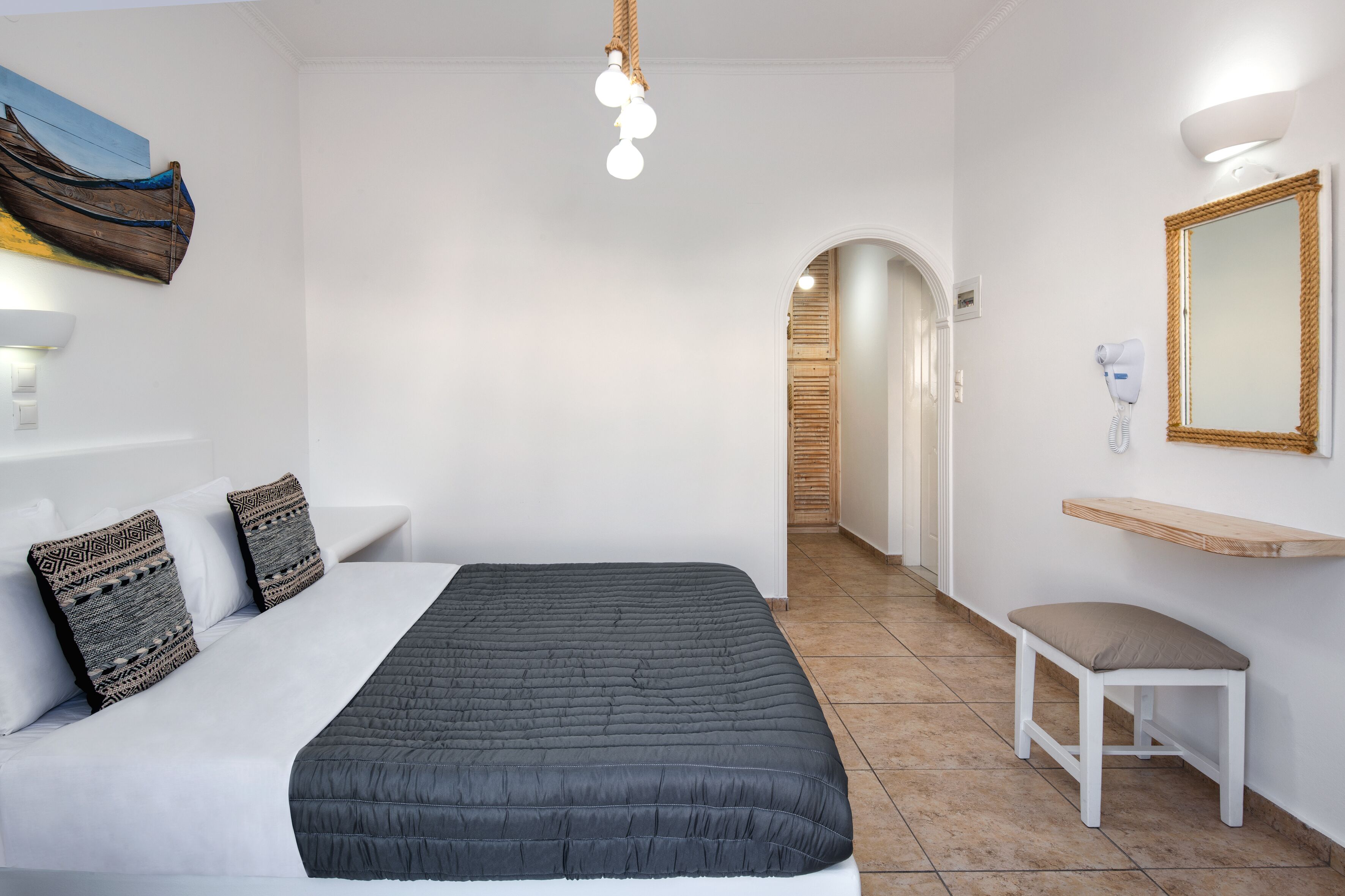 A bedroom with a bed, bedside lamp, wall-mounted mirror, and a bench.